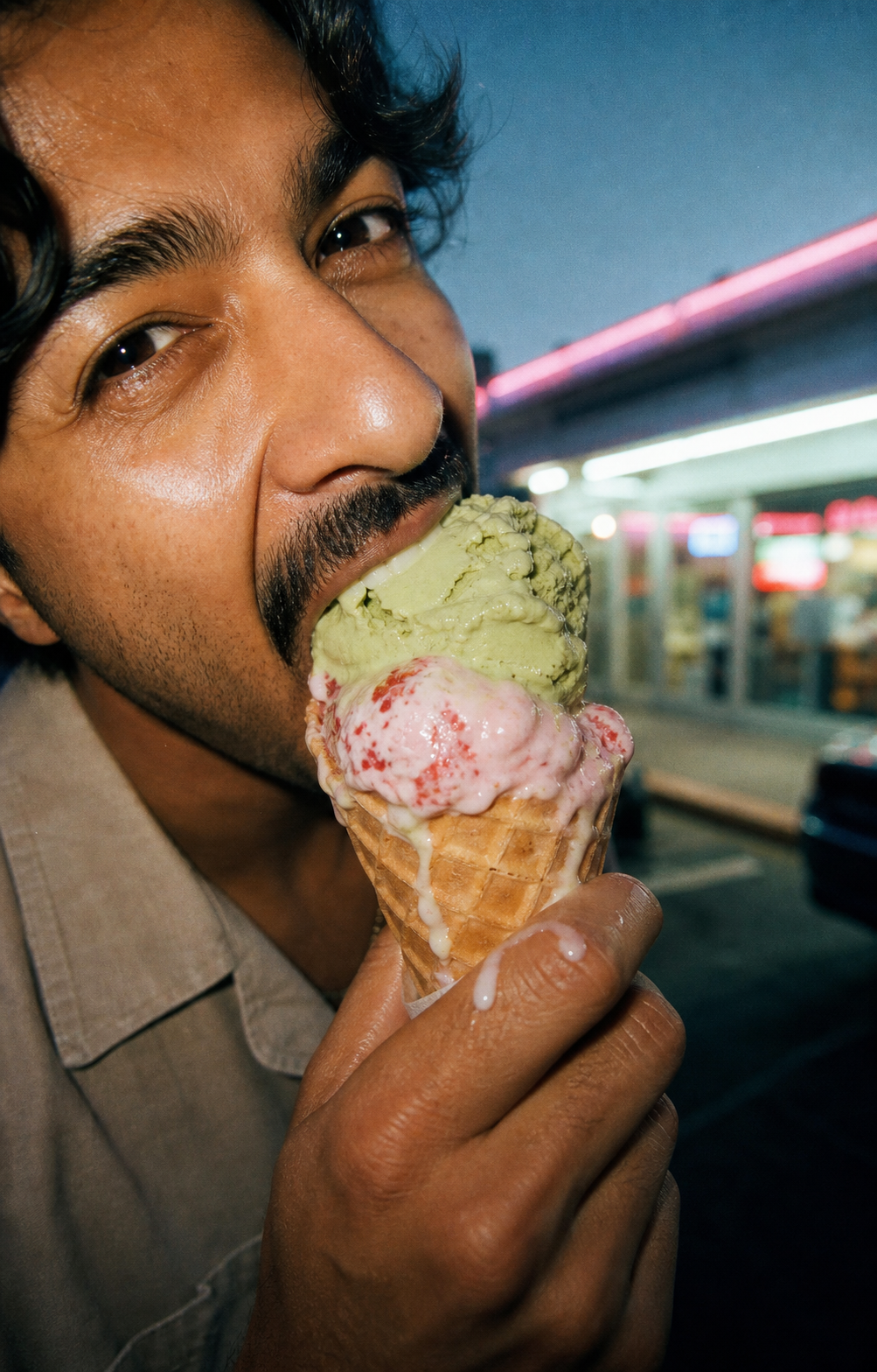 Close-up of someone eating a melting double-scoop ice cream cone at night.